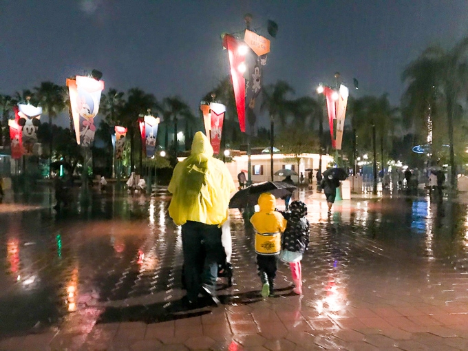 A man and his two children walking through Disneyland in the rain.