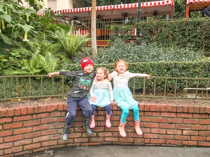 Three kids sitting on a half wall at Disneland in Winter.