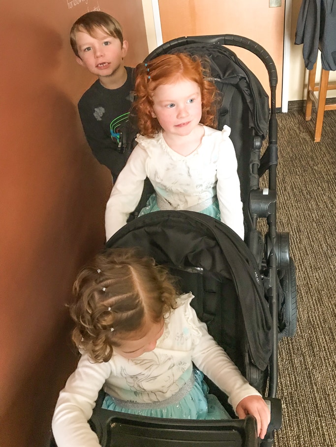 Three kids riding on a City Select Double stroller (with glider board) during a trip to Disneyland in Winter.