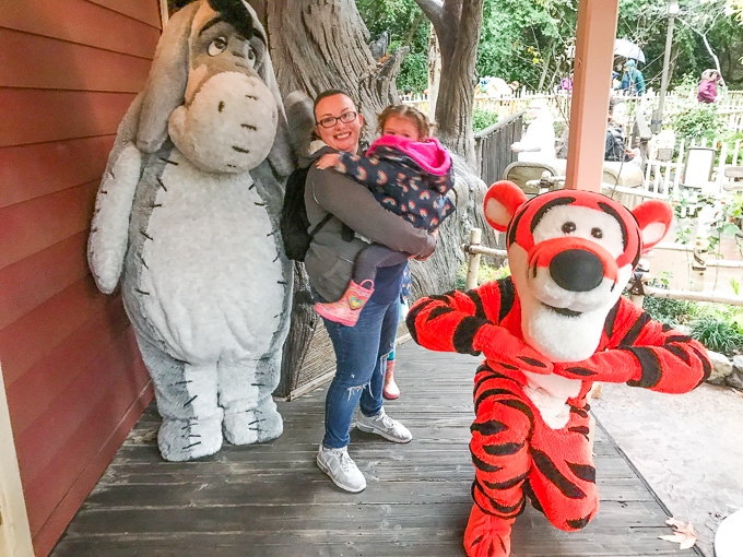 A little girl in her mom's arms next to Winne the Pooh and Tigger at Disneyland in Winter.