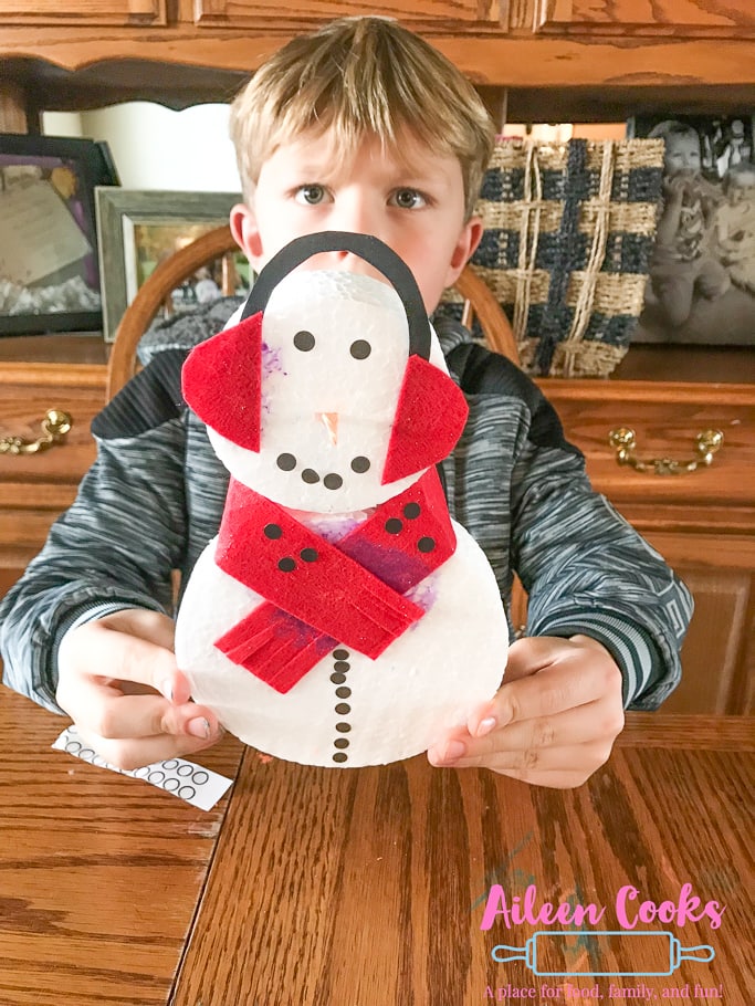 A boy holding a foam snowman with red ear muffs made from the Winter themed We Craft Box.
