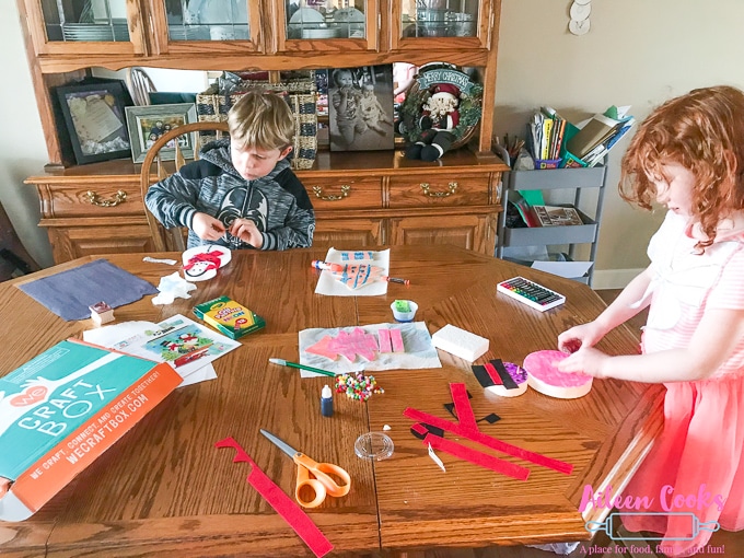 Two children sitting at a wooden table make winter crafts from We Craft Box.