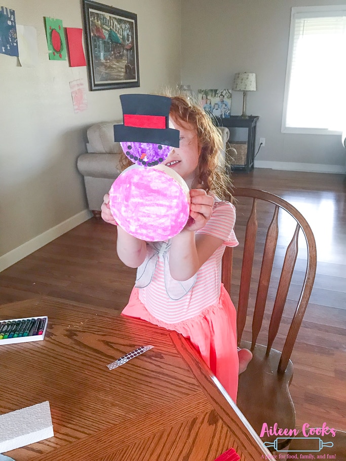 A girl holding up a pink colored foam snowman with top hat from We Craft Box.