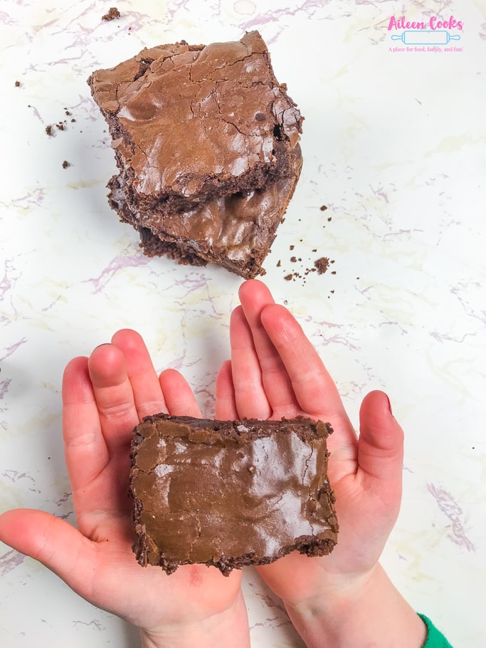 A child's hands holding a chocolate chunk brownie.