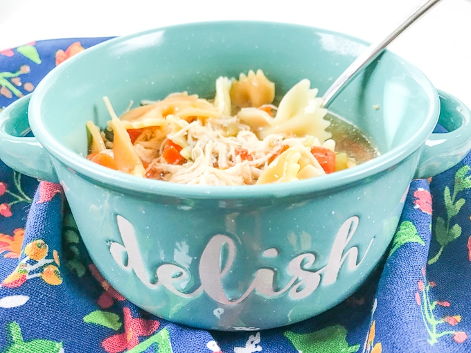 A teal bowl with the words "delish" written on the front and filled with the instant pot chicken noodle soup recipe.