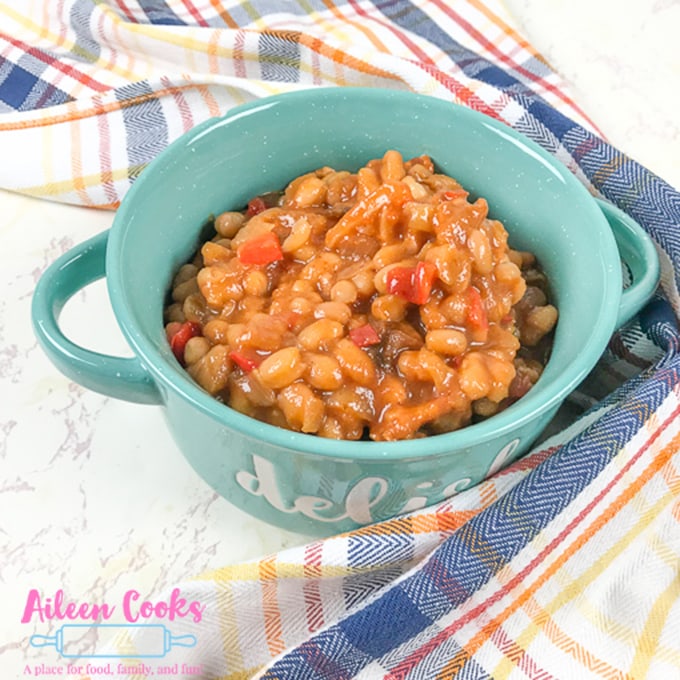A plaid towel next to a blue bowl filled with instant pot baked beans.