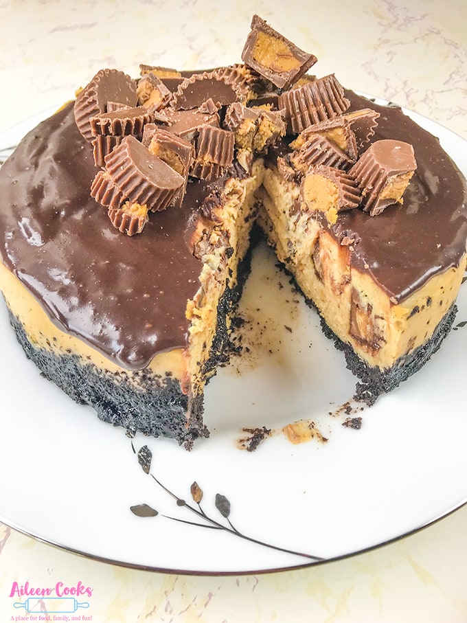 A peanut butter chocolate cheesecake with one slice cut out, showing the Reese's peanut butter cups inside the cheesecake.