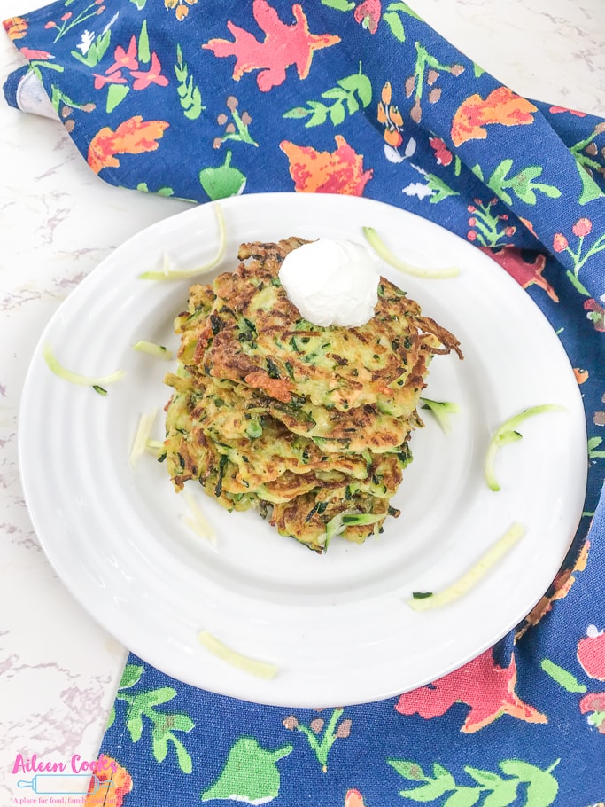 A plate of zucchini fritters next to a blue floral dish towel.