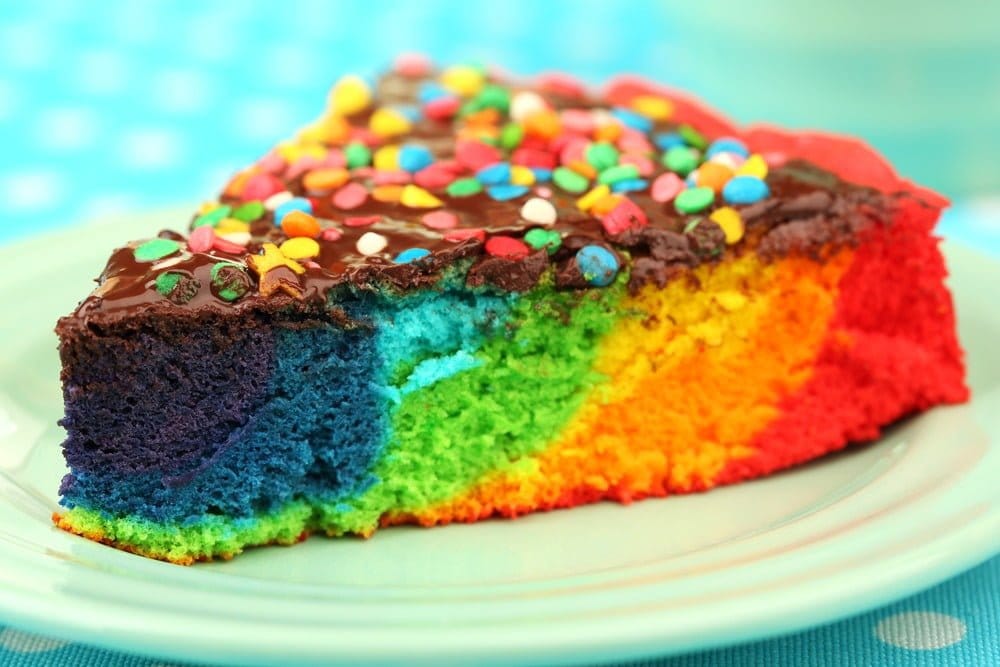 A slice of cake colored in tie-die and topped with colorful candies.