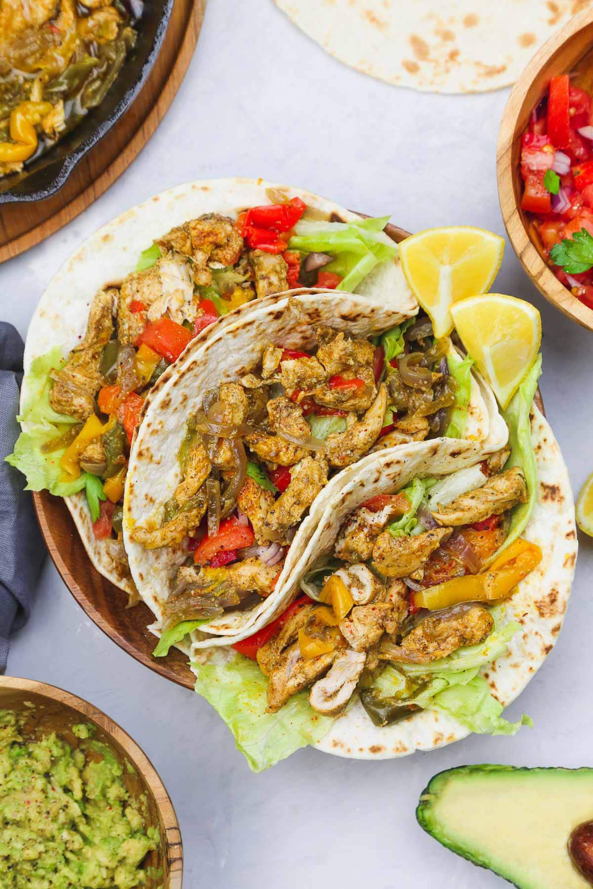 A plate with three chicken fajitas topped with lime and lettuce.