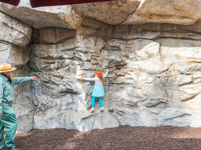 A red-headed girl climbing sideways on a rock wall.