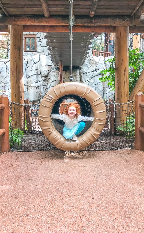 A little girl poking her head out of the tunnel at the Redwood Creek Challenge Trail inside Disney California Adventure Park.
