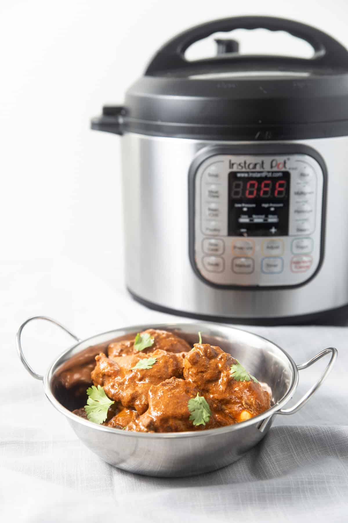 A bowl of butter chicken in front of an Instant Pot.