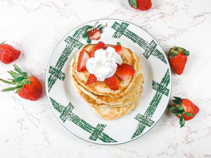 A plate with apples painted on it holding a stack of pancakes.