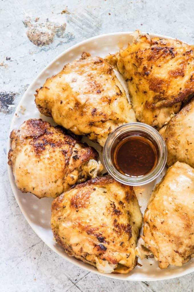 A large plate with chicken thighs around a small glass bowl of sauce.