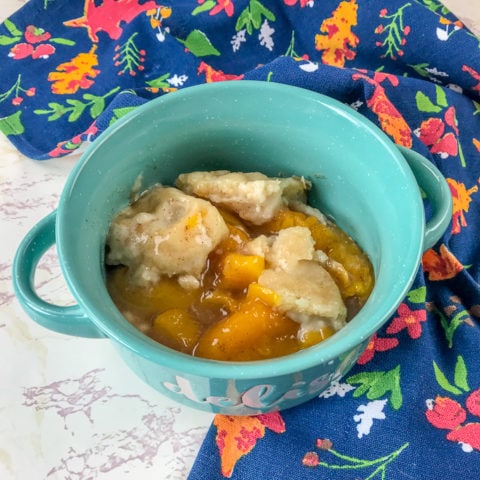 Instant pot peach cobbler in a blue bowl, on top of a blue and orange dish towel.