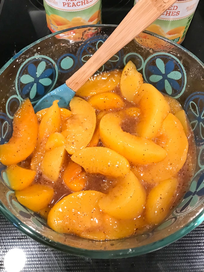 Peaches mixed with sugars in a cake pan.