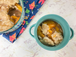 Bowl of instant pot peach cobbler with cake pan of peach cobbler in upper left hand corner.