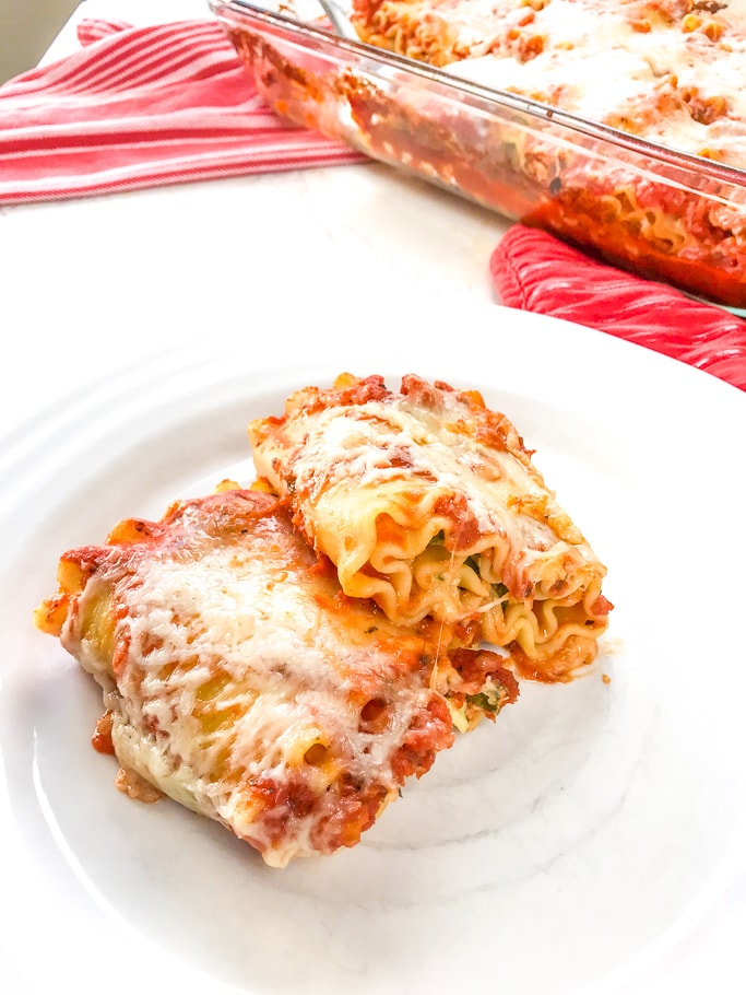 A close-up of two spinach lasagna rolls on a white plate.