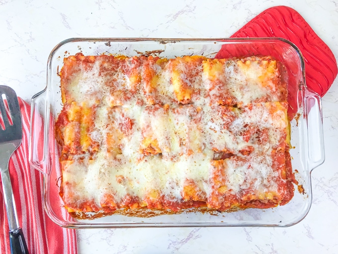 A casserole dish filled with spinach lasagna roll-ups recipe on top of a red oven mitt.
