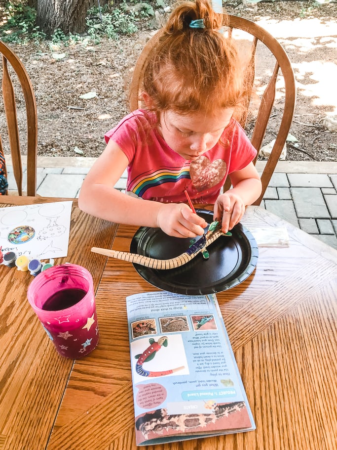 A little girl painting a wooden lizard.