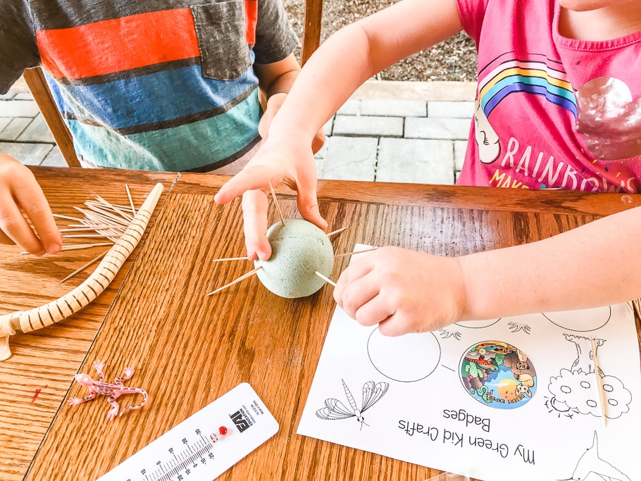 Two sets of hands poking toothpicks into a foam ball.