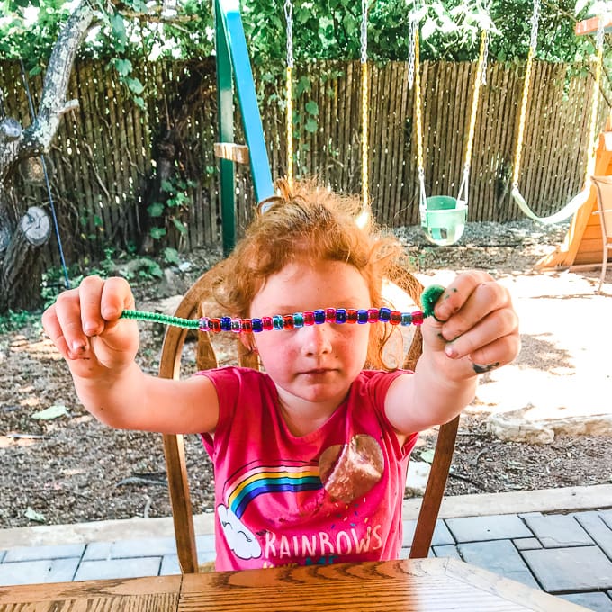 A little girl holding up a pattern snake made from colorful beads and a pipe cleaner.