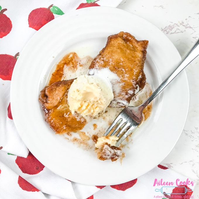 A white plate with two apple dumplings topped with vanilla ice cream.