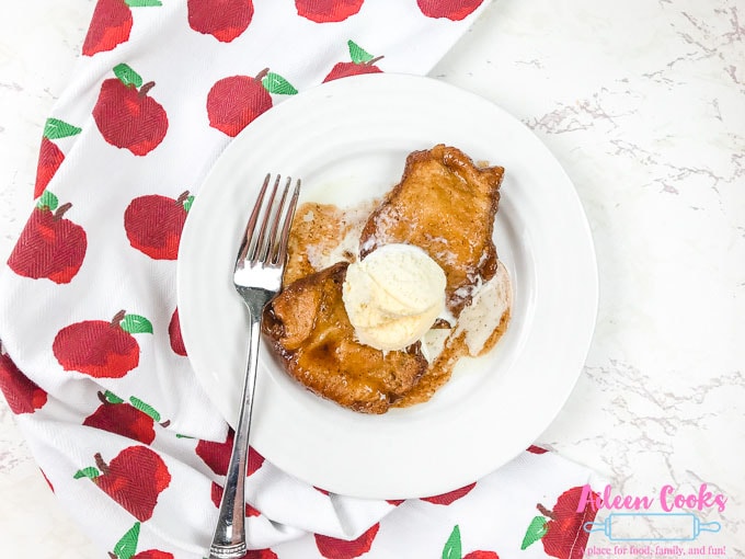 A plate of two instant pot apple dumplings under a scoop of vanilla ice cream.