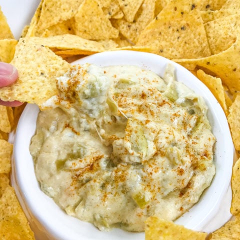 A hand holding a chip with instant pot artichoke dip on top.