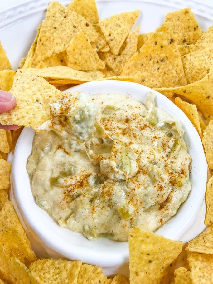 A hand holding a chip with instant pot artichoke dip on top.