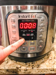 A finger pointing to a button on the instant pot.