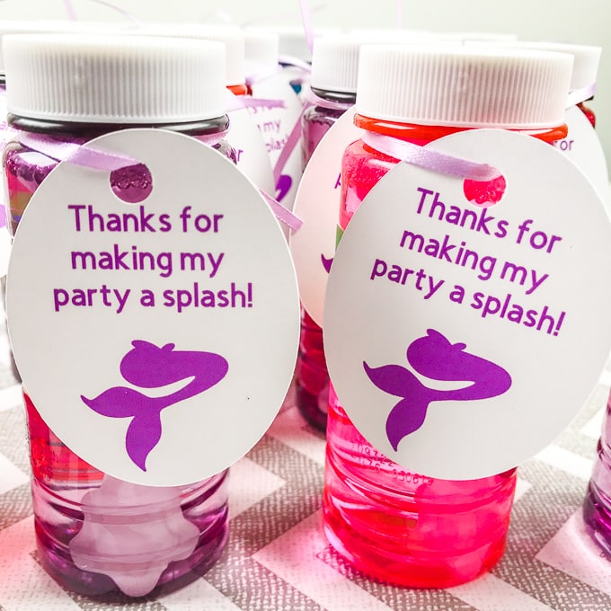 Two bottles of bubbles with mermaid favor tags tied on with purple ribbon.