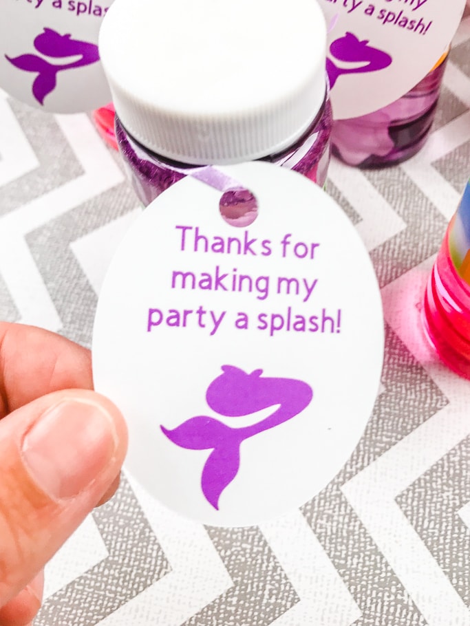 A hand holding on to a mermaid favor tag attached to a bottle of bubbles.