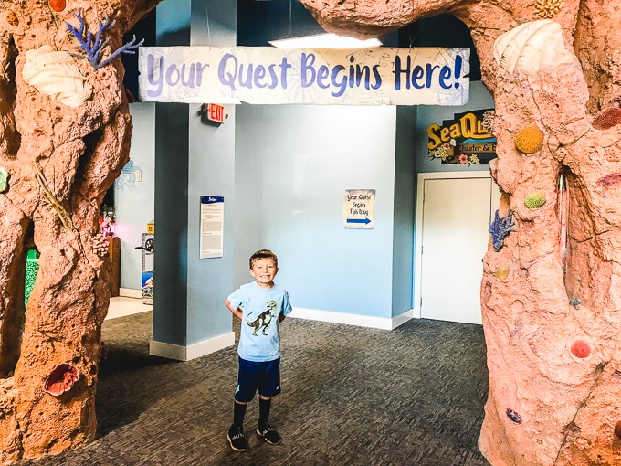 A boy posing in front of a sign that says "Your Adventure Starts Here".