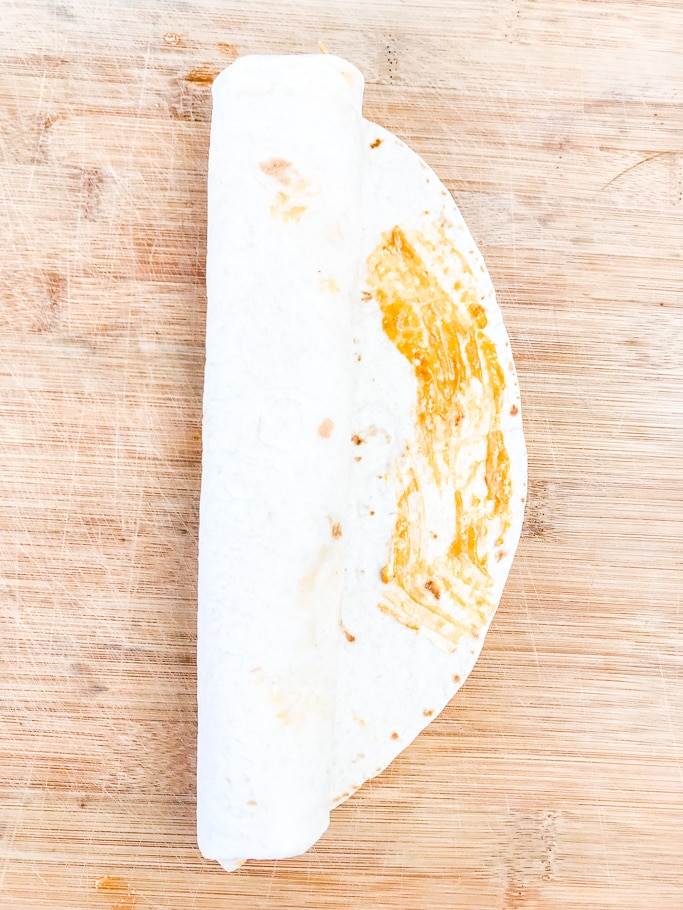 A tortilla rolled up with sauce on one edge.