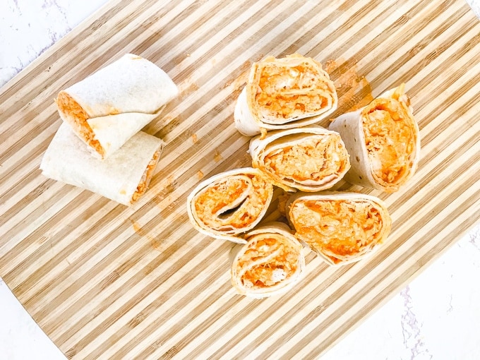 A striped cutting board filled with buffalo chicken roll-ups.