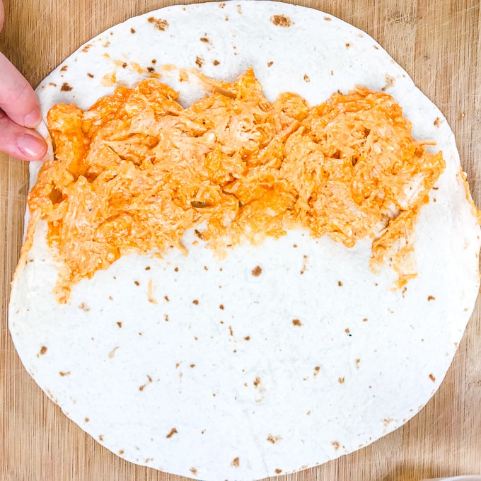 A large flour tortilla with buffalo chicken spread on half of it.