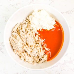 A white bowl filled with shredded chicken, cream cheese, and buffalo sauce.