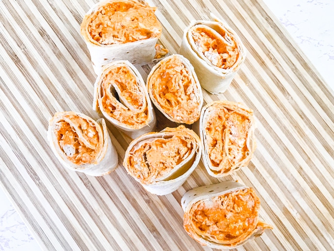 A close up of buffalo chicken roll-ups on a striped cutting board.