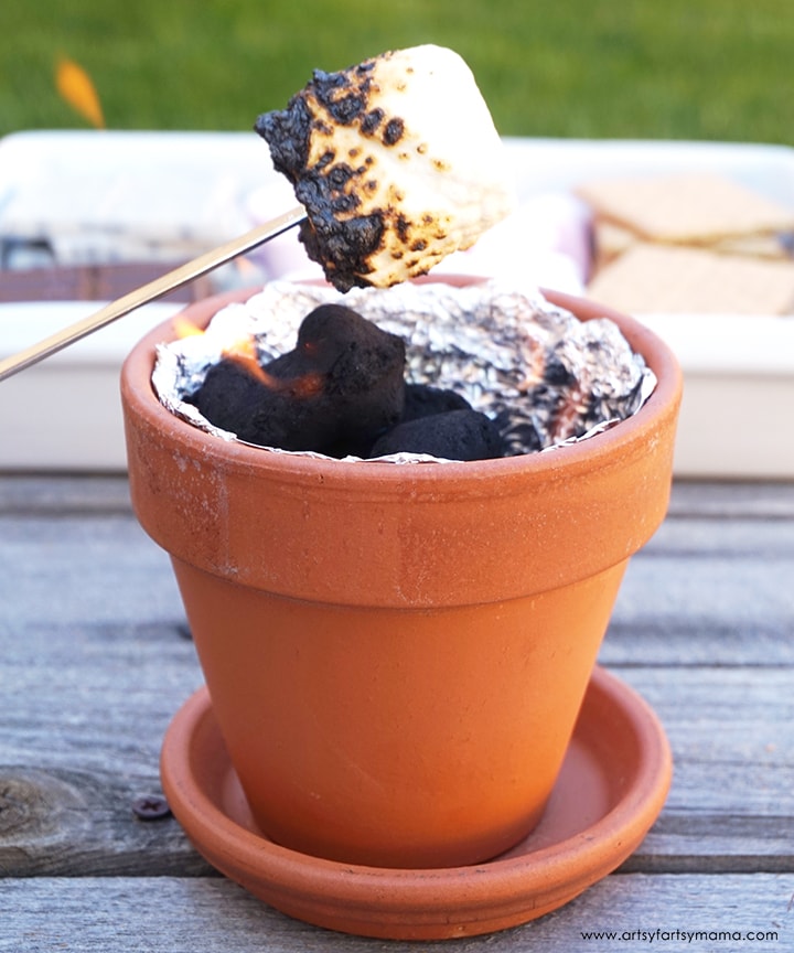 A marshmallow being roasted over a mini campfire in a pot.