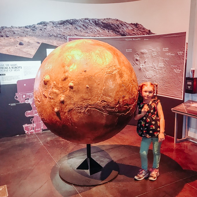 A girl standing next to a large model of Mars.