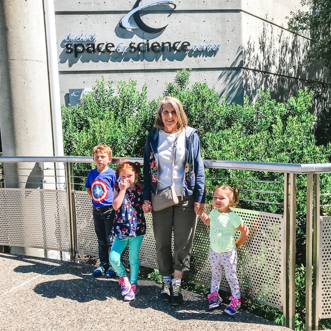 A woman standing with her three grandchildren in front of Oakland's Chabot Space & Science Center.