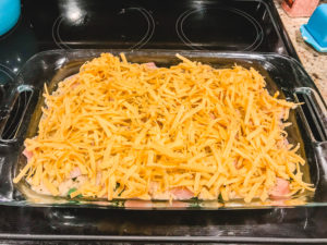A casserole dish layered with red potatoes, green beans, chicken, béchamel sauce, and shredded cheese.