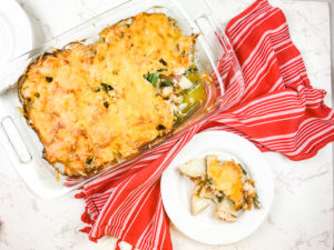 A plate of chicken and potato casserole next to the casserole dish.