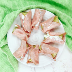 Ham and cream cheese roll-ups with pickle next to a green towel.