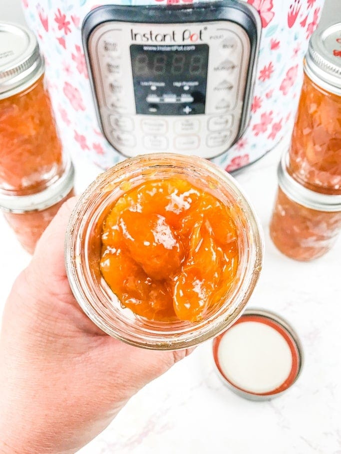 A hand holding an open jar of instant pot apricot jam.