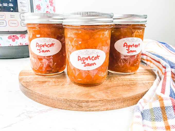 Three jars of apricot jam on a wooden platform.