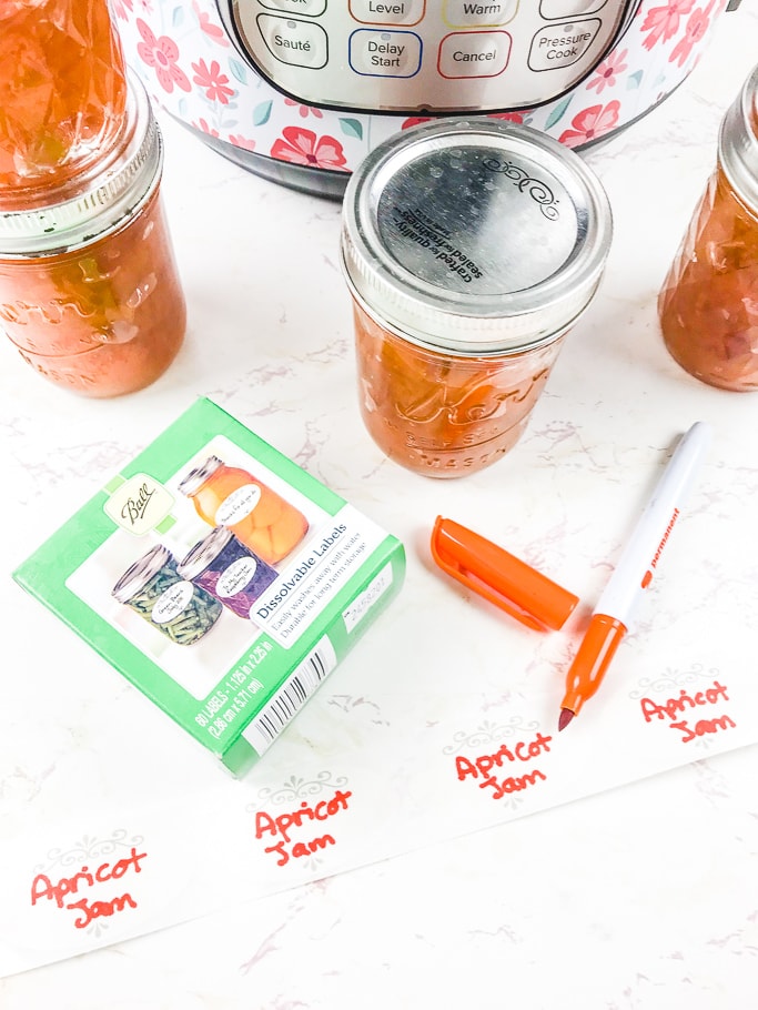 A jar of peach jam next to Ball Dissolvable labels and an orange permanent marker.