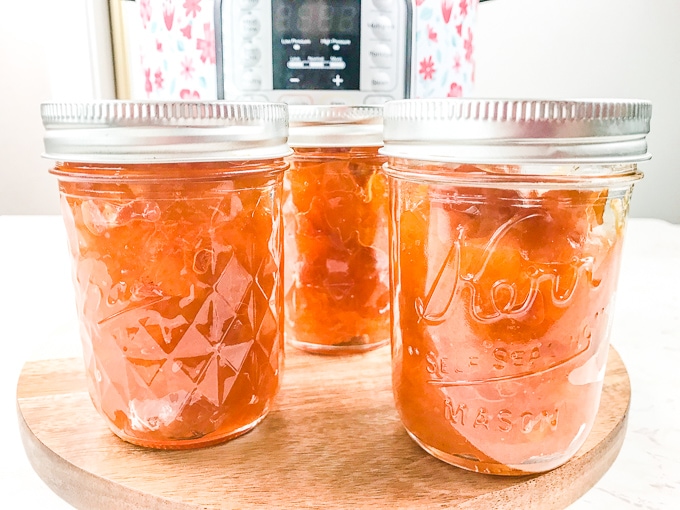 Three jars of instant pot peach jam in front of an Instant Pot.